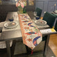 Narrow table runner with gingerbread and stocking pattern and a red tassel on a dining table, not an option design