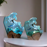 Two ocean wave resin lamps with surfer and whale shark lit on a white side table