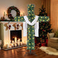 Green cross shaped Christmas tree with warm white lights and a white cloth beside a fireplace with stockings