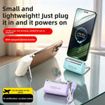 Capsule power banks charging phones on a glass table, one phone resting upright on a fold-out stand