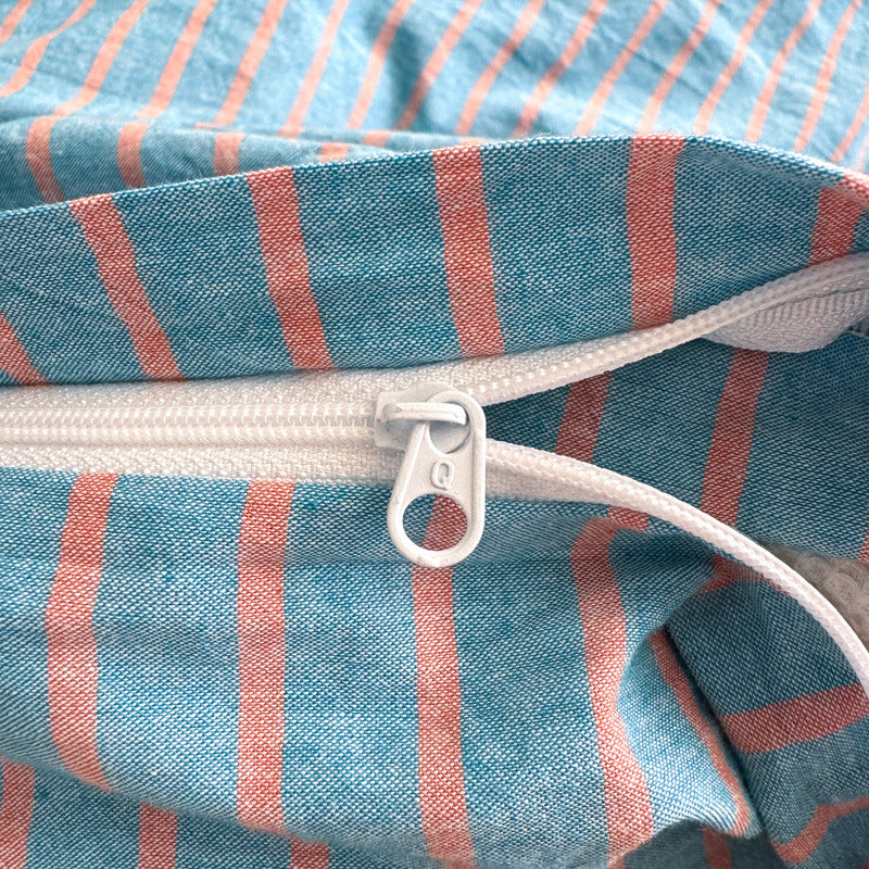 Zipper opening on a blue and coral striped cotton quilt cover, close up of the white zip and pull