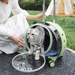Green pet carrier with a transparent bubble window opened while a cat steps out beside a seated woman on grass