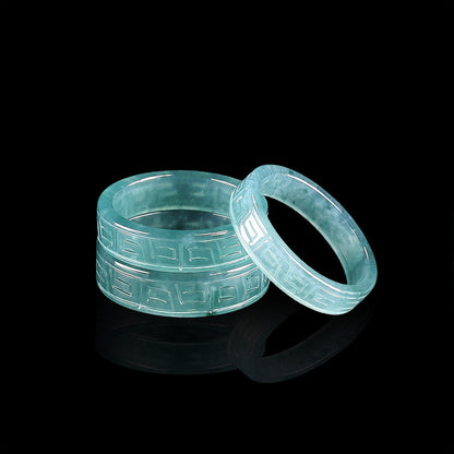 Two blue water jadeite band rings with a carved antique fret pattern on a black ground