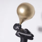 Close view of the balloon and folded arms of the black figure sculpture against a plain studio background