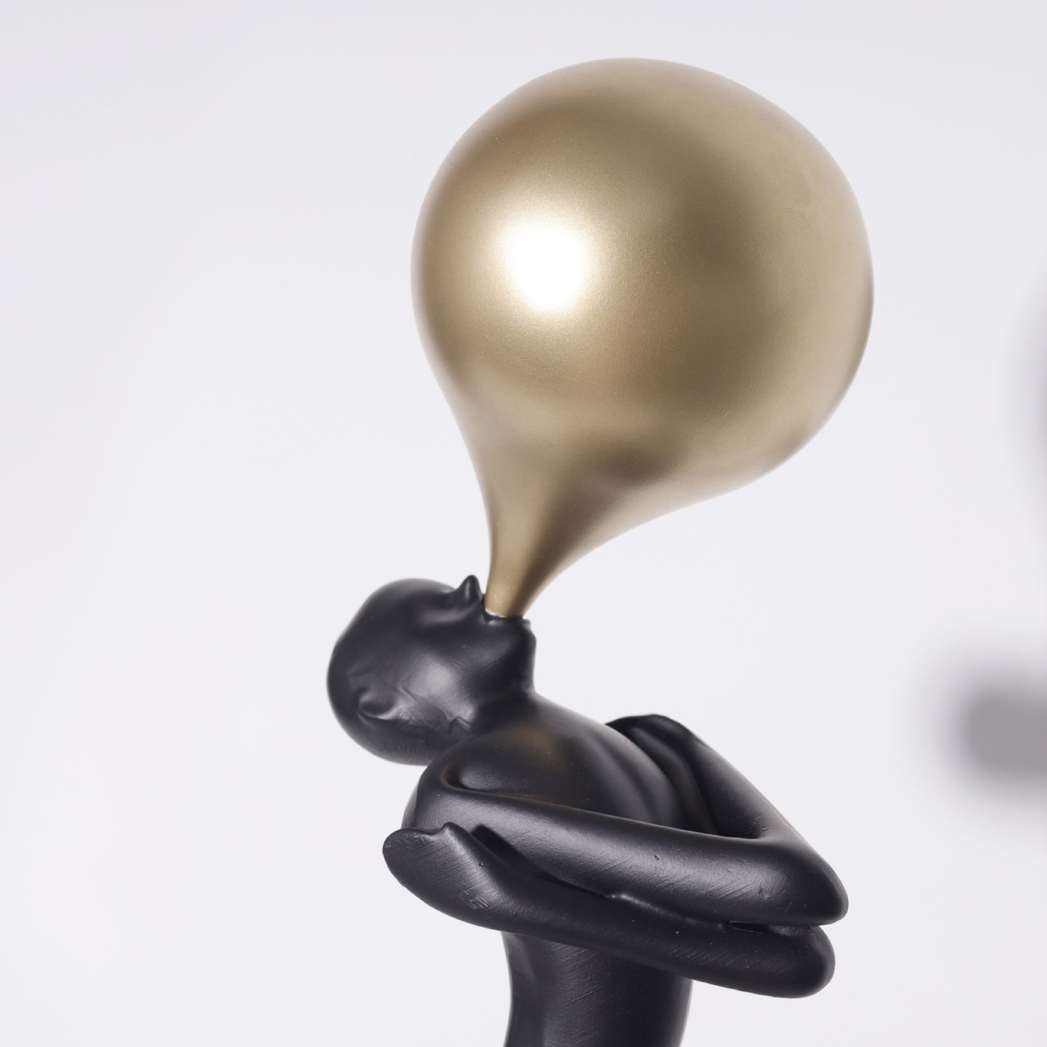 Close view of the balloon and folded arms of the black figure sculpture against a plain studio background