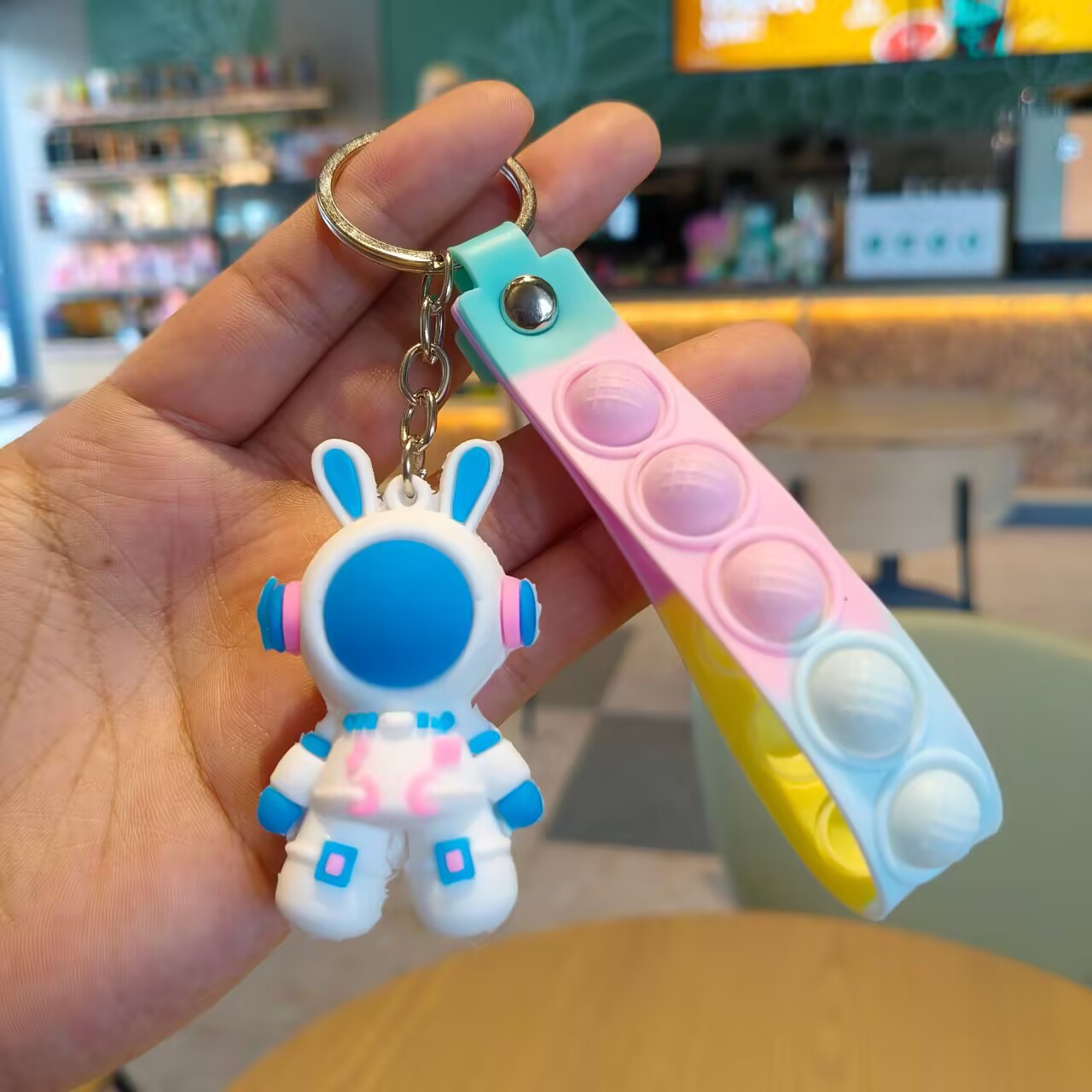 Single blue helmet astronaut rabbit charm on a pink and yellow silicone pop strap held in a hand
