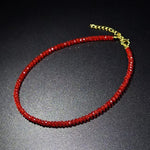 Red faceted glass bead choker necklace with a gold tone extension chain on a dark surface