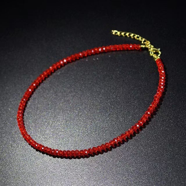 Red faceted glass bead choker necklace with a gold tone extension chain on a dark surface