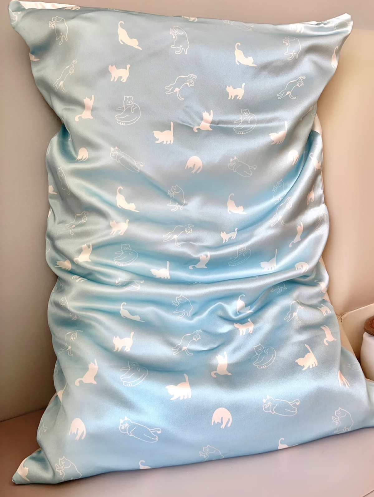 Sky blue kitten print silk pillowcase with small cat motifs on a chair