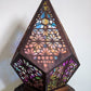 Faceted boho table lamp with pierced floral shade glowing multicolor in a dim room
