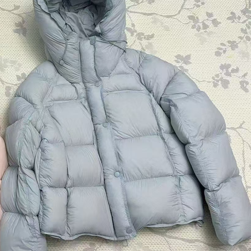 Close up of the light blue puffer hood, drawcord and snap button placket over the front zip