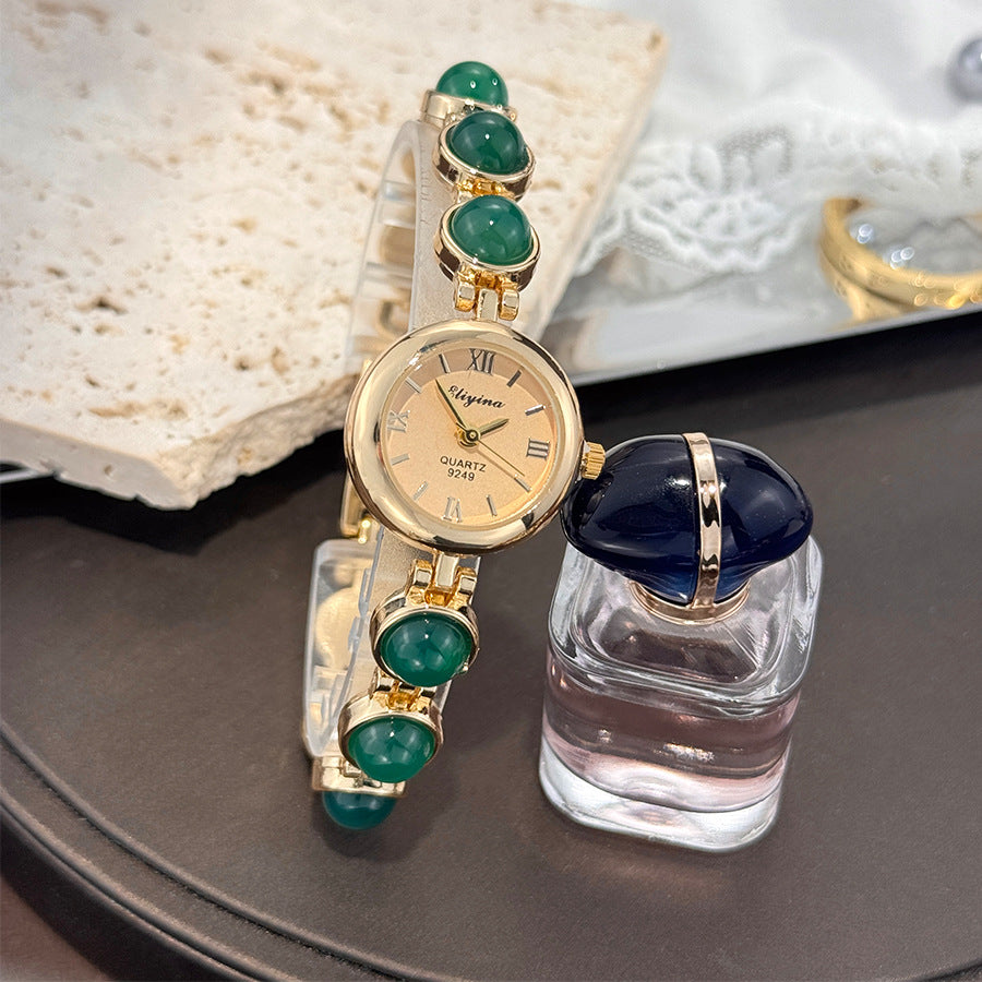 Gold tone quartz watch on a mixed stone and metal bead bracelet, flat lay