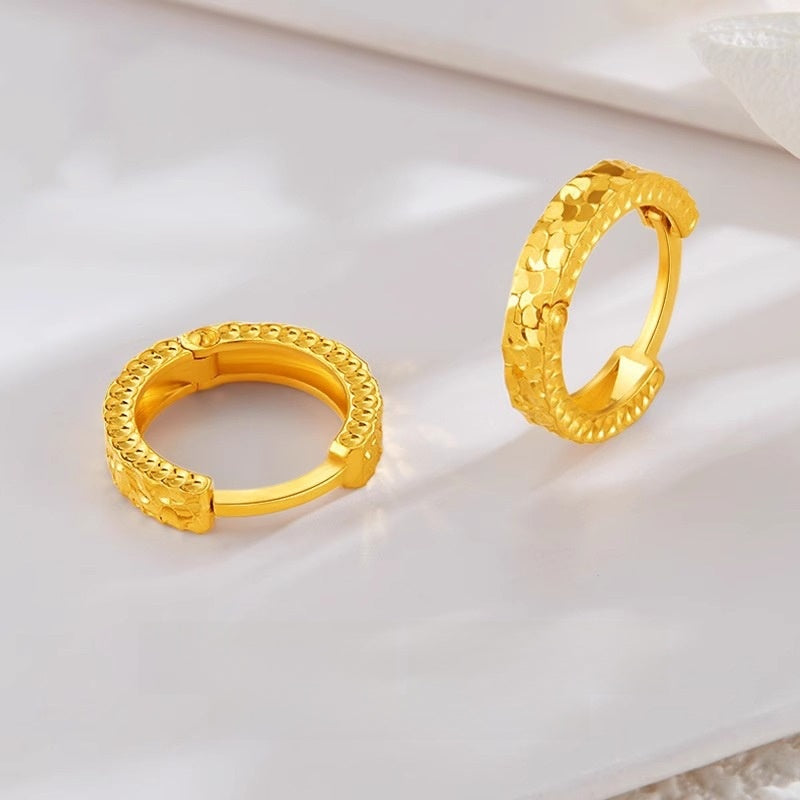 Two gold-plated huggie hoop earrings, one lying open to show the hinge and one standing, on a pale marble surface