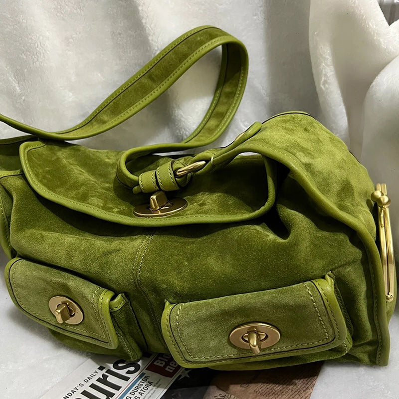 Olive green suede shoulder bag with a flap, twist lock and front pockets beside a white fur cloth