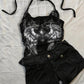 Black halter top with silver wing print and lace shoulder panels laid flat beside black cuffed shorts