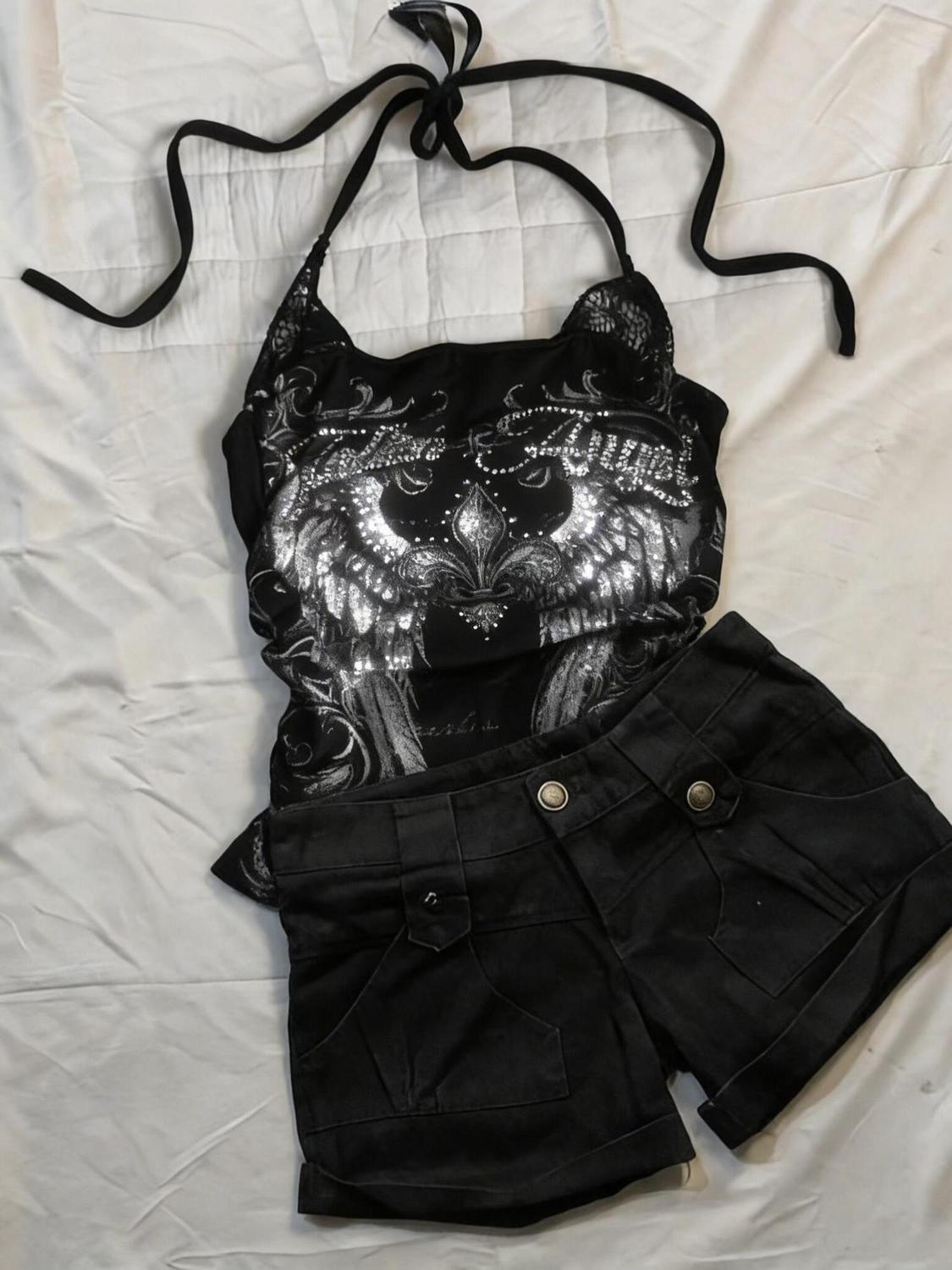Black halter top with silver wing print and lace shoulder panels laid flat beside black cuffed shorts
