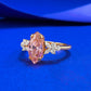 Side profile of the ring on blue silk, pink marquise stone between two clear petal clusters