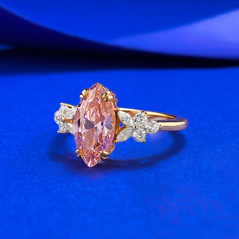 Side profile of the ring on blue silk, pink marquise stone between two clear petal clusters