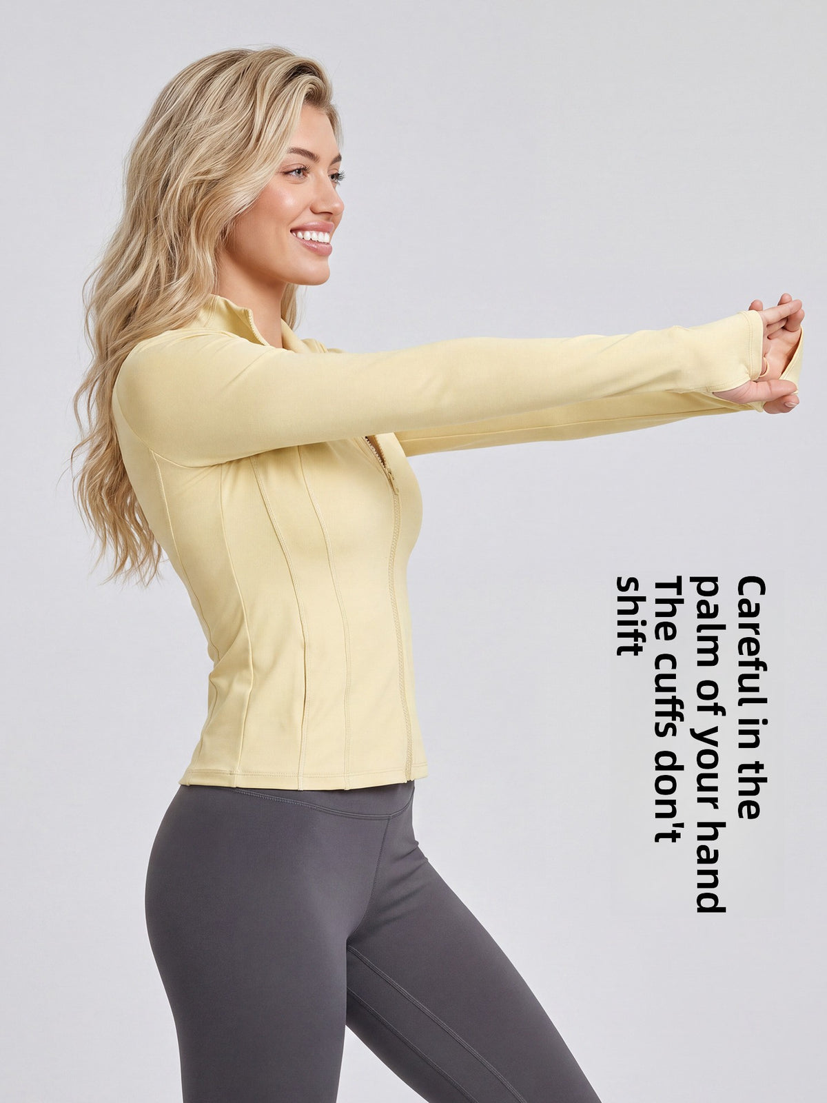 Woman in a yellow stand collar zip jacket reaching one arm forward, side view showing the thumb holes