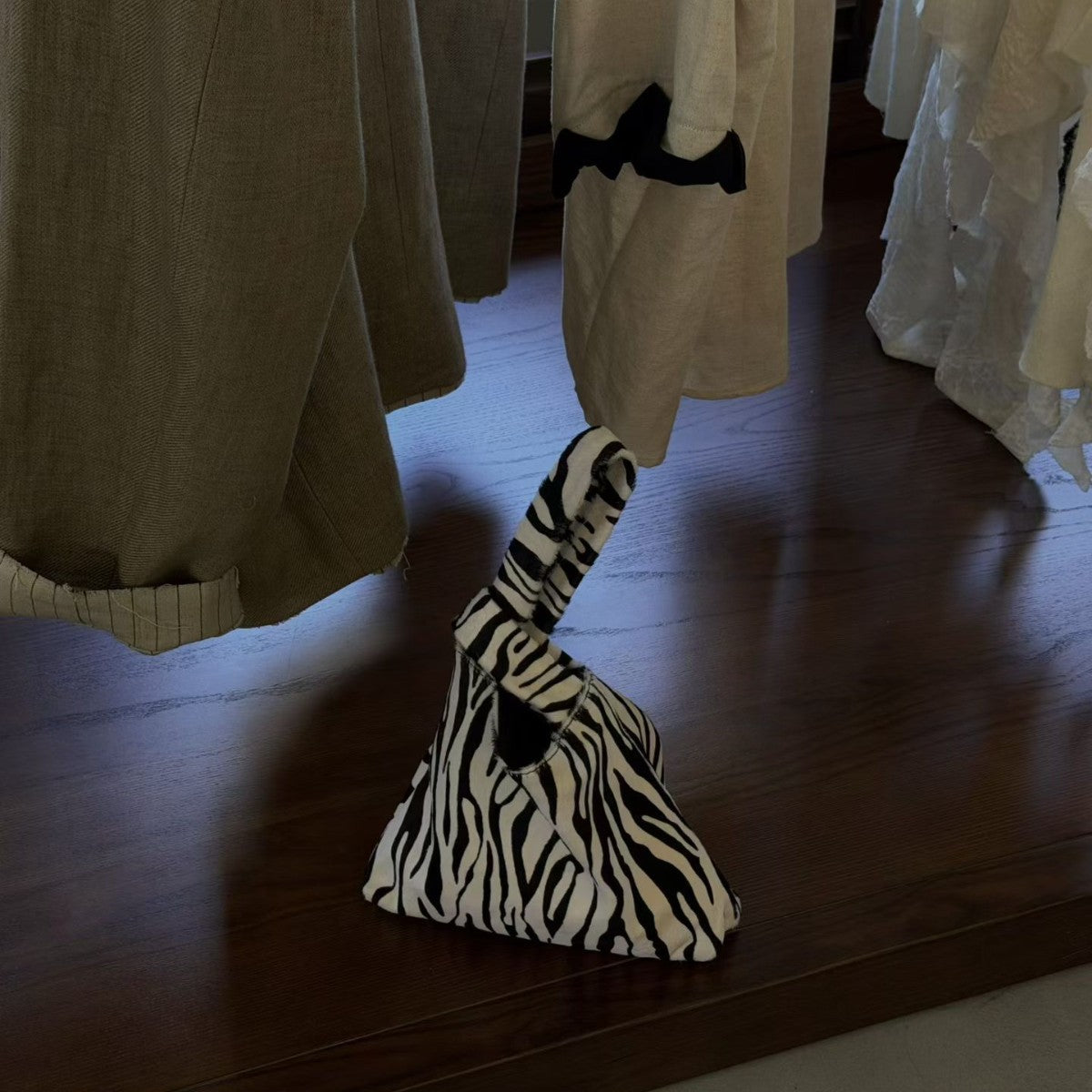 Zebra stripe triangle knot handle pouch bag standing on a wooden table beside linen clothing