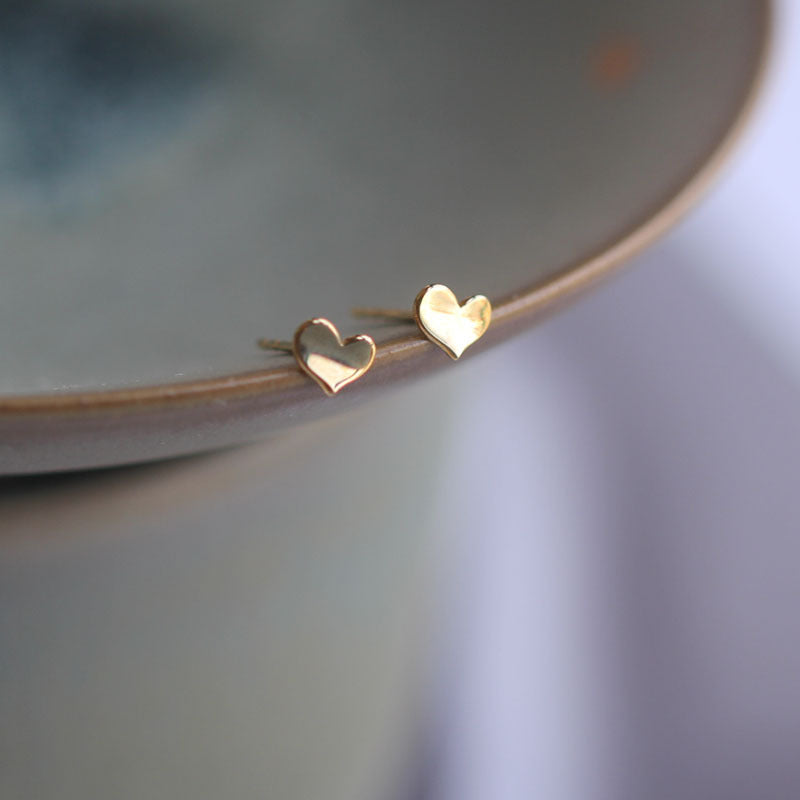 Top down layout of the gold-tone 3D wave heart earring on a plain surface