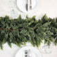 Green cedar garland running down the centre of a set dining table between white plates and glasses