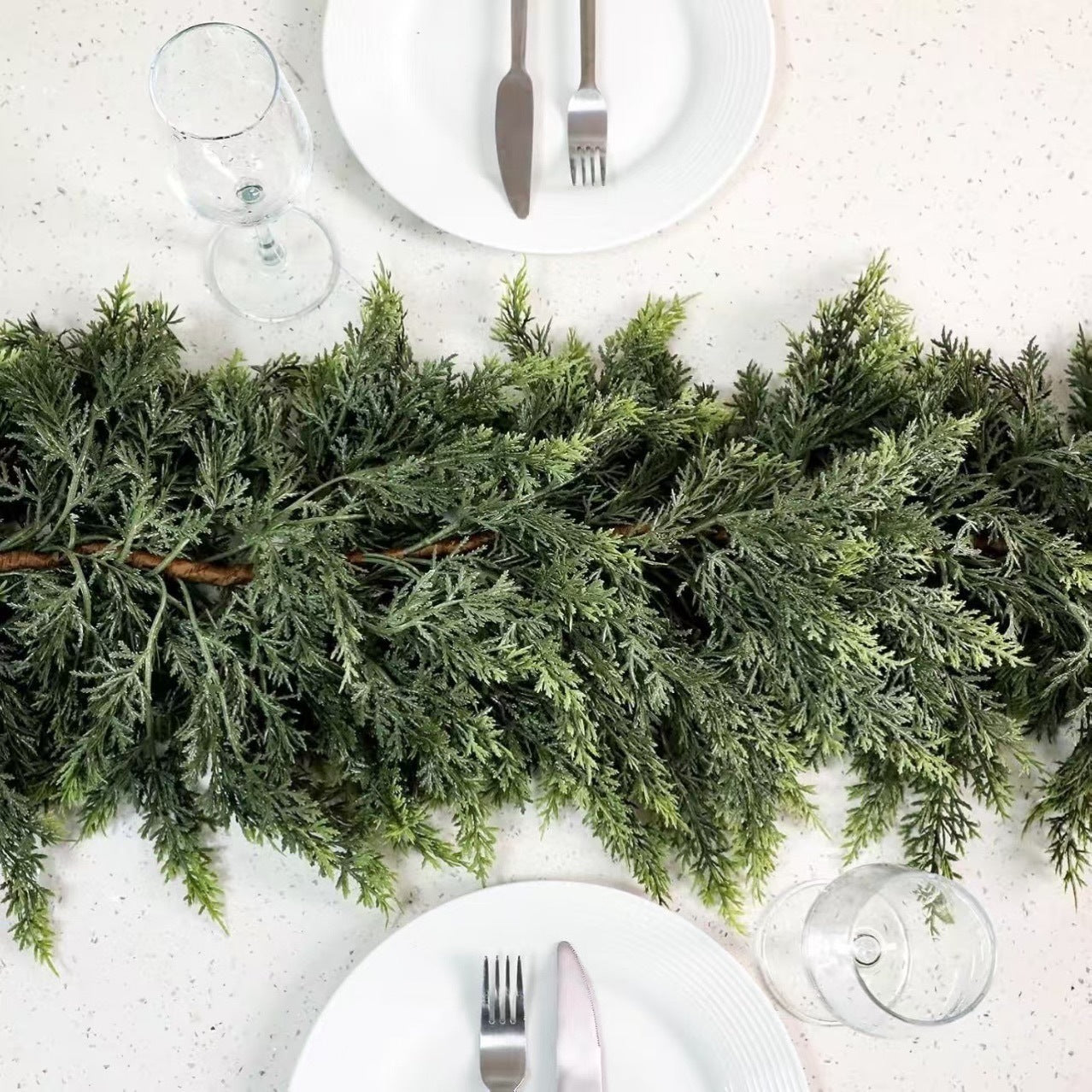 Green cedar garland running down the centre of a set dining table between white plates and glasses