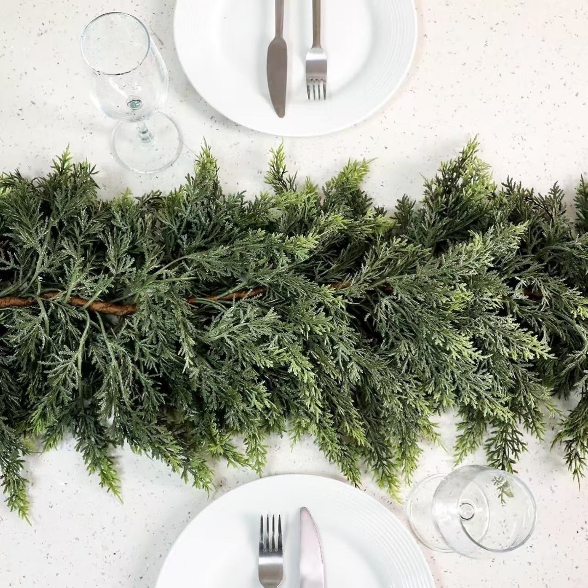 Green cedar garland running down the centre of a set dining table between white plates and glasses
