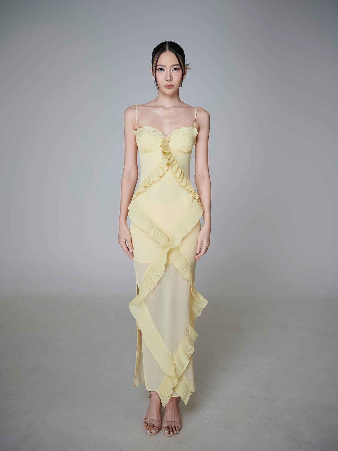 Light yellow spaghetti strap maxi dress on a model, pleated ruffle bands crossing the sheer skirt to a pointed hem