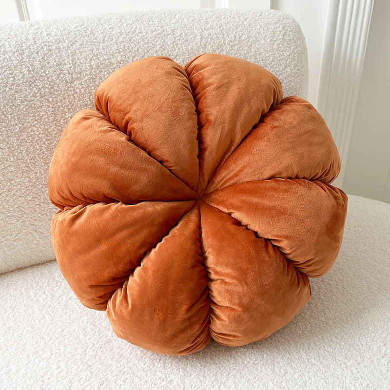 Orange eight-petal plush pumpkin throw pillow on a white boucle chair, orange eight-petal bud variant