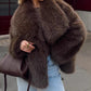 Woman in a dark brown vegan fur jacket with glasses and a brown bag, in light blue jeans on a street