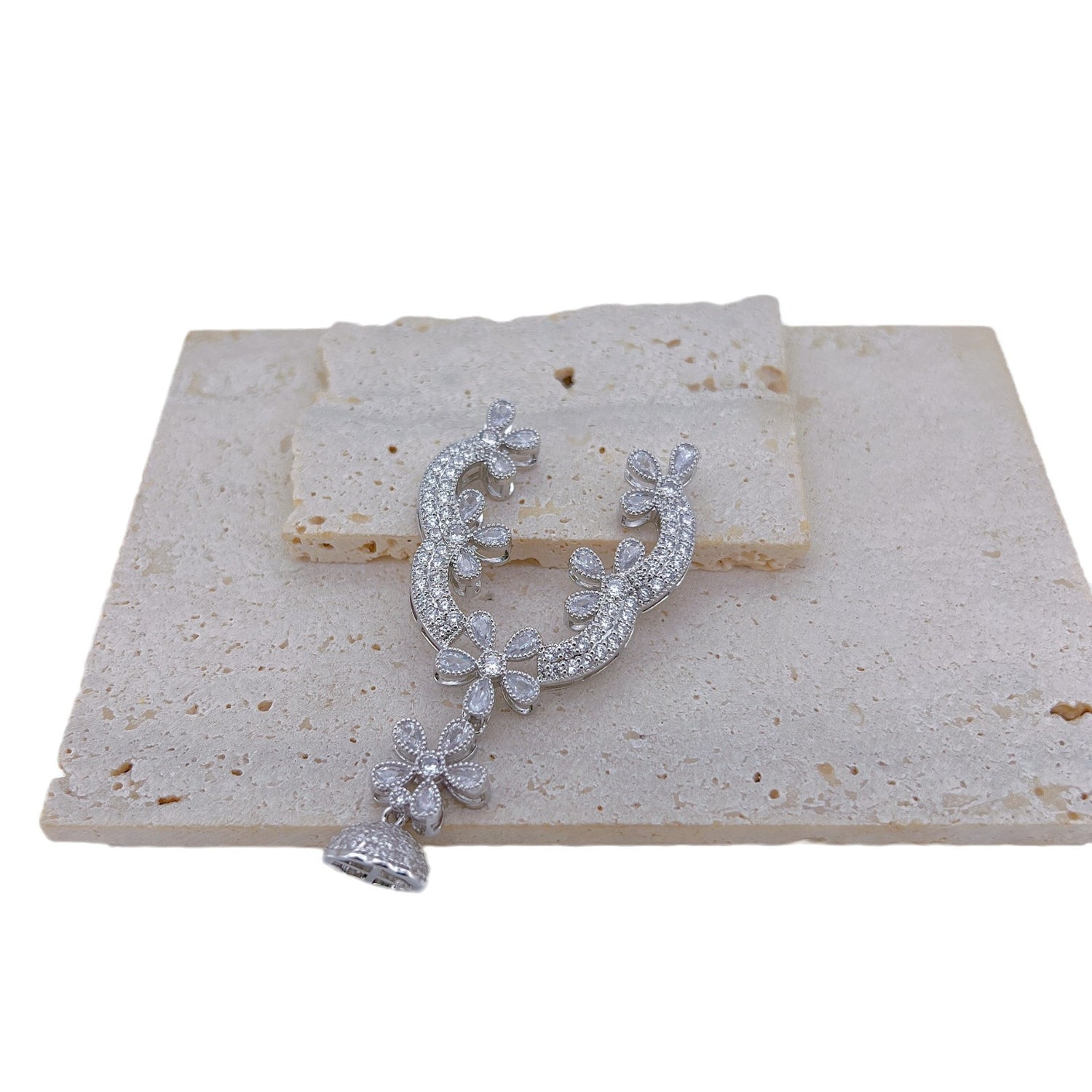 Silver tone rhinestone floral connector with its domed tassel cap bail, shown alone on a stone tile