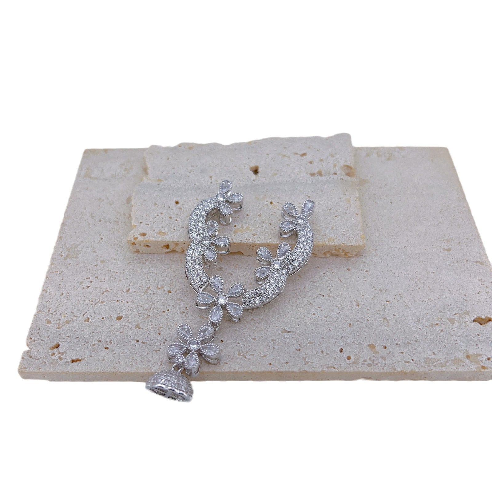 Silver tone rhinestone floral connector with its domed tassel cap bail, shown alone on a stone tile