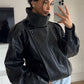 Woman taking a mirror selfie in a black PU leather moto jacket with a snapped stand collar and shoulder straps