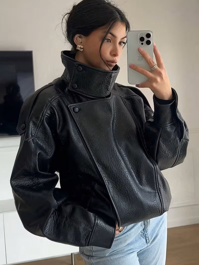 Woman taking a mirror selfie in a black PU leather moto jacket with a snapped stand collar and shoulder straps