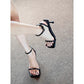 Foot wearing a black square toe ankle strap sandal with thin heel and buckle on a beige mat