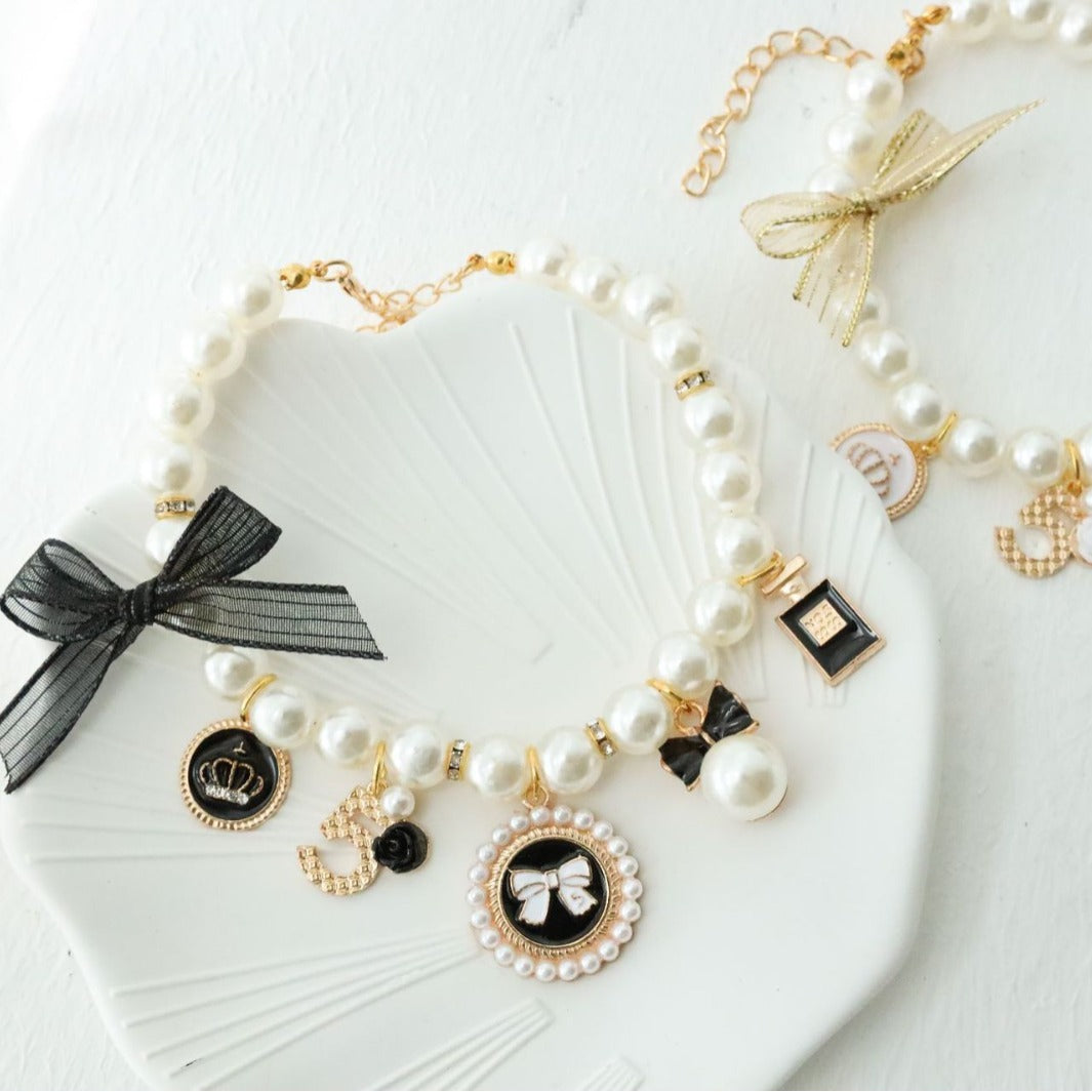Faux pearl beaded pet collar with gold tone charms and a small bell, styled on a white shell dish