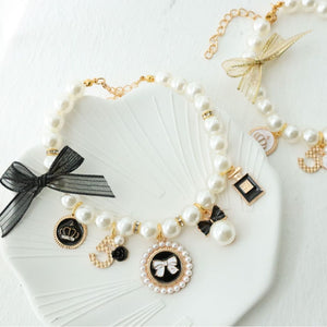 Faux pearl beaded pet collar with gold tone charms and a small bell, styled on a white shell dish