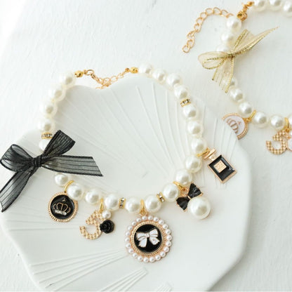 Faux pearl beaded pet collar with gold tone charms and a small bell, styled on a white shell dish