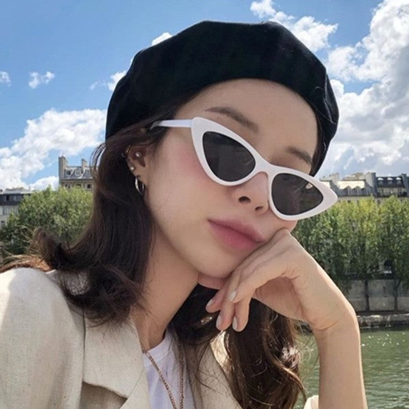 Woman in a black beret wearing white framed triangular cat eye sunglasses outdoors