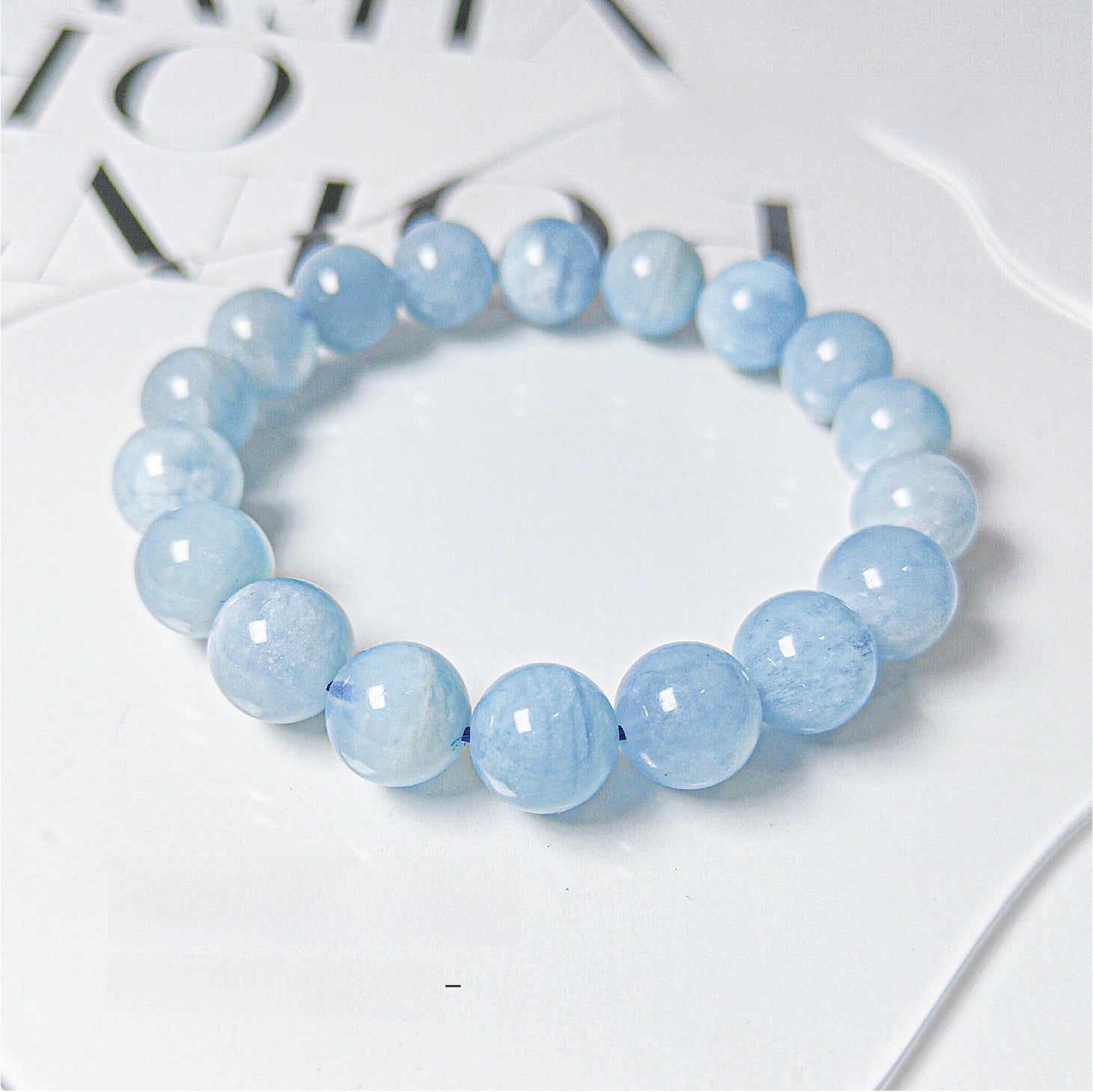 Aquamarine blue bead stretch bracelet on a white magazine, round milky blue polished stone beads