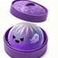 Purple ghost squishy dumpling toy in a purple steamer with the woven look lid propped open