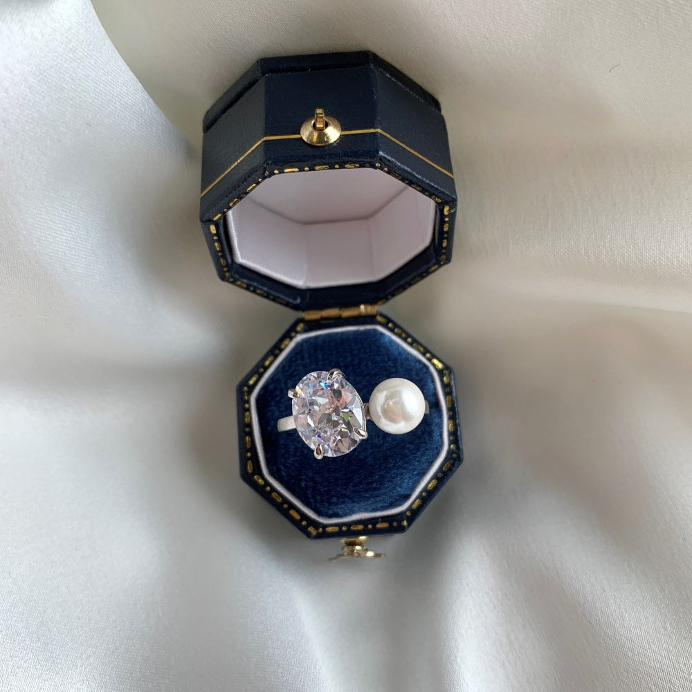 Open silver ring set in a navy velvet box, cubic zirconia and imitation pearl side by side