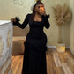 Woman in a black long sleeve maxi dress with ruffled cuffs, hip rosettes and a mesh skirt taking a mirror selfie