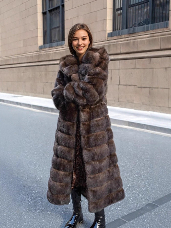Woman in a long brown vegan fur coat held closed in front, hood down, standing on a street