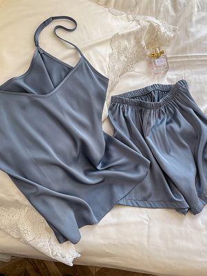 Satin cami and shorts pajama set laid flat with a perfume bottle and lace trim