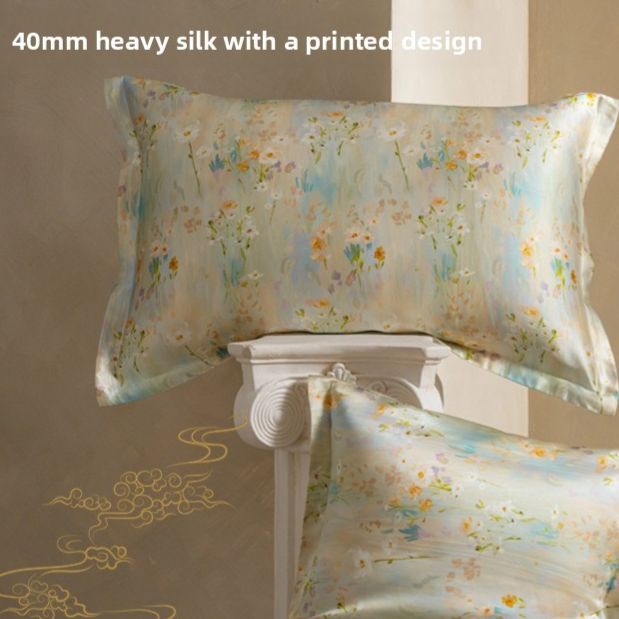 Silk pillowcase printed with pastel wildflowers on a beige ground, shown with a second case on a stone pedestal