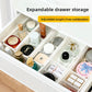 Open drawer neatly divided by several white extendable organizer boxes holding small items