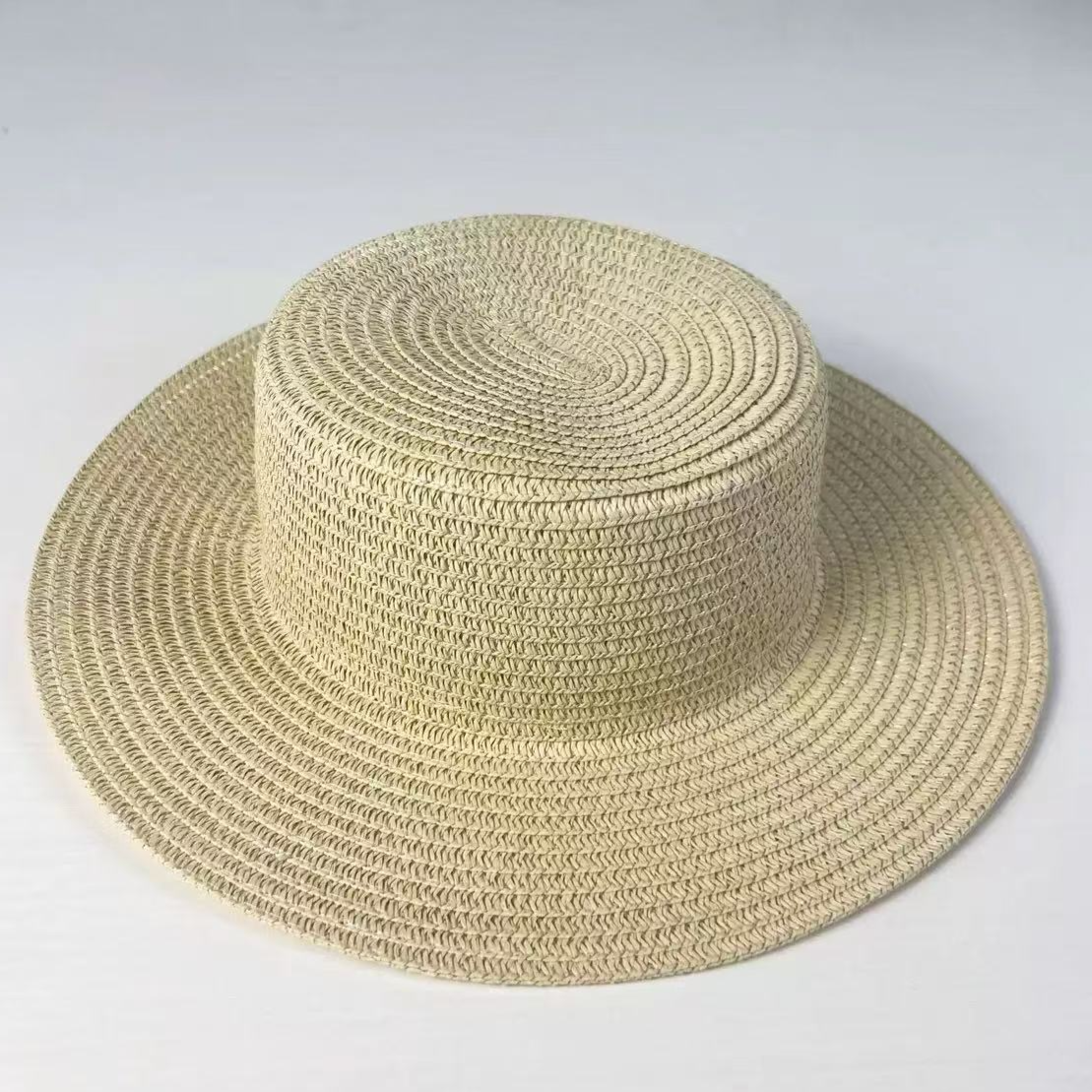 Top view of a woven straw sun hat showing the spiral braid of the flat crown