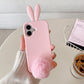 Light pink rabbit ear silicone iPhone case held in hand with fluffy pom pom tail